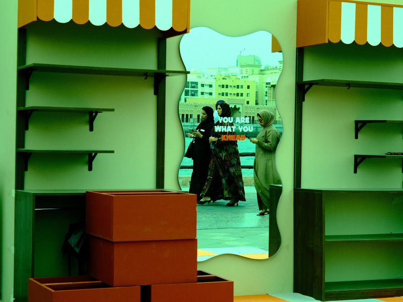 A reflective mirror in a colorful market setting showing people interacting, with shelves and boxes around.