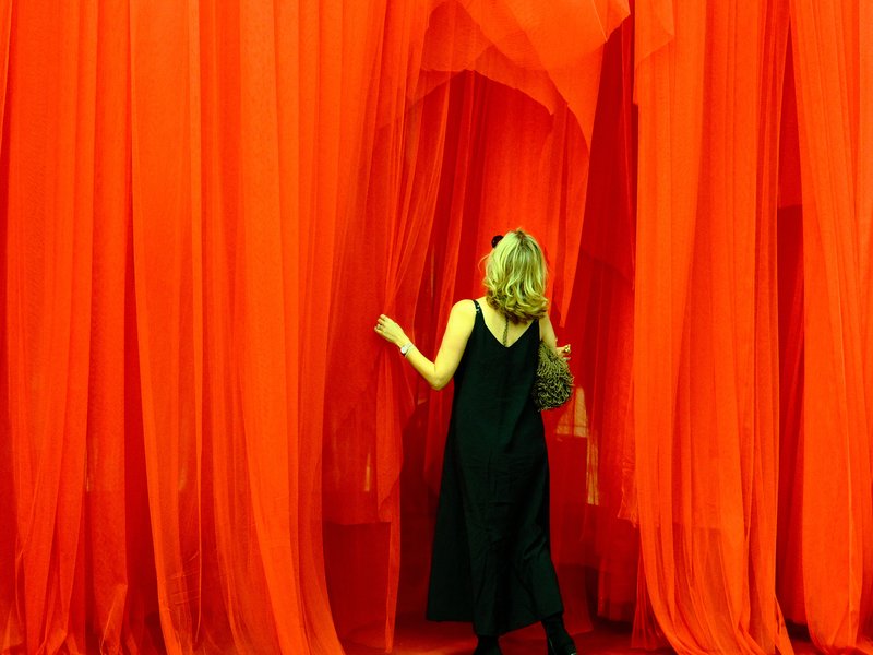 A woman in a black dress walking through flowing red fabric curtains in a vibrant indoor space.