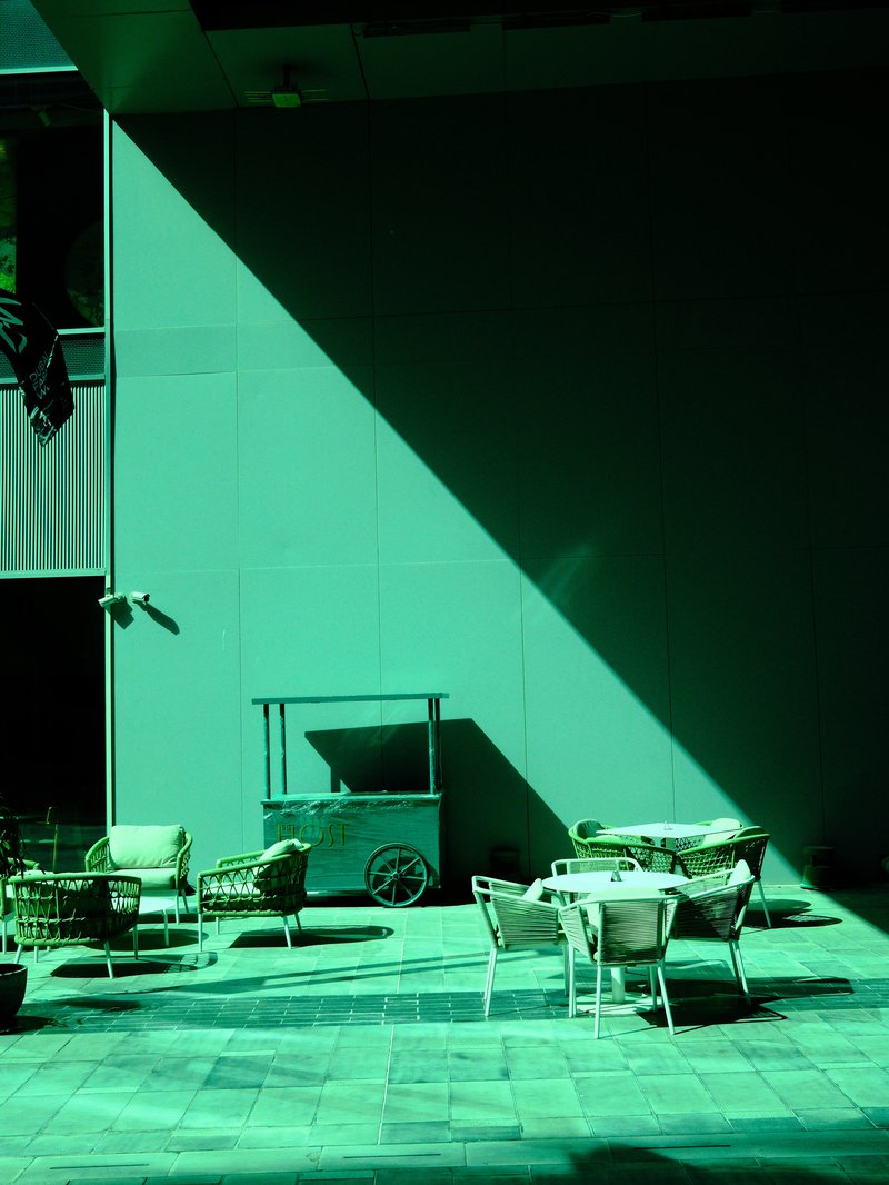 A shadowed outdoor seating area with white furniture against a green wall.