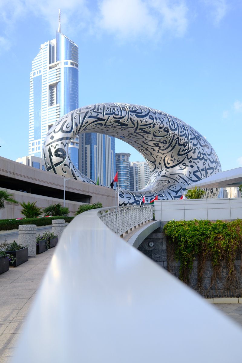 A futuristic building with Arabic calligraphy design in an urban setting, surrounded by modern skyscrapers.