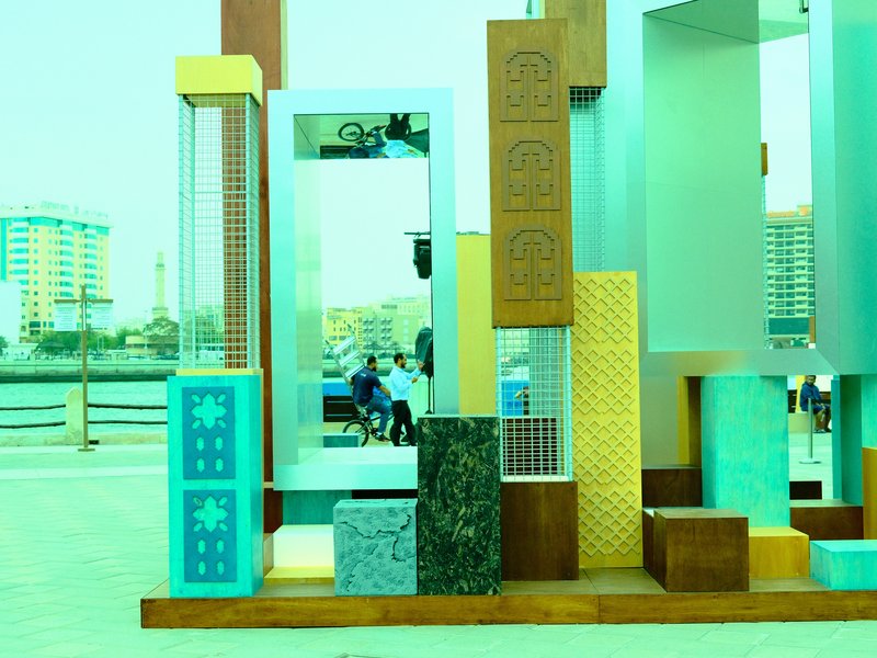 Colorful abstract sculpture with various geometric shapes and textures in an urban setting.