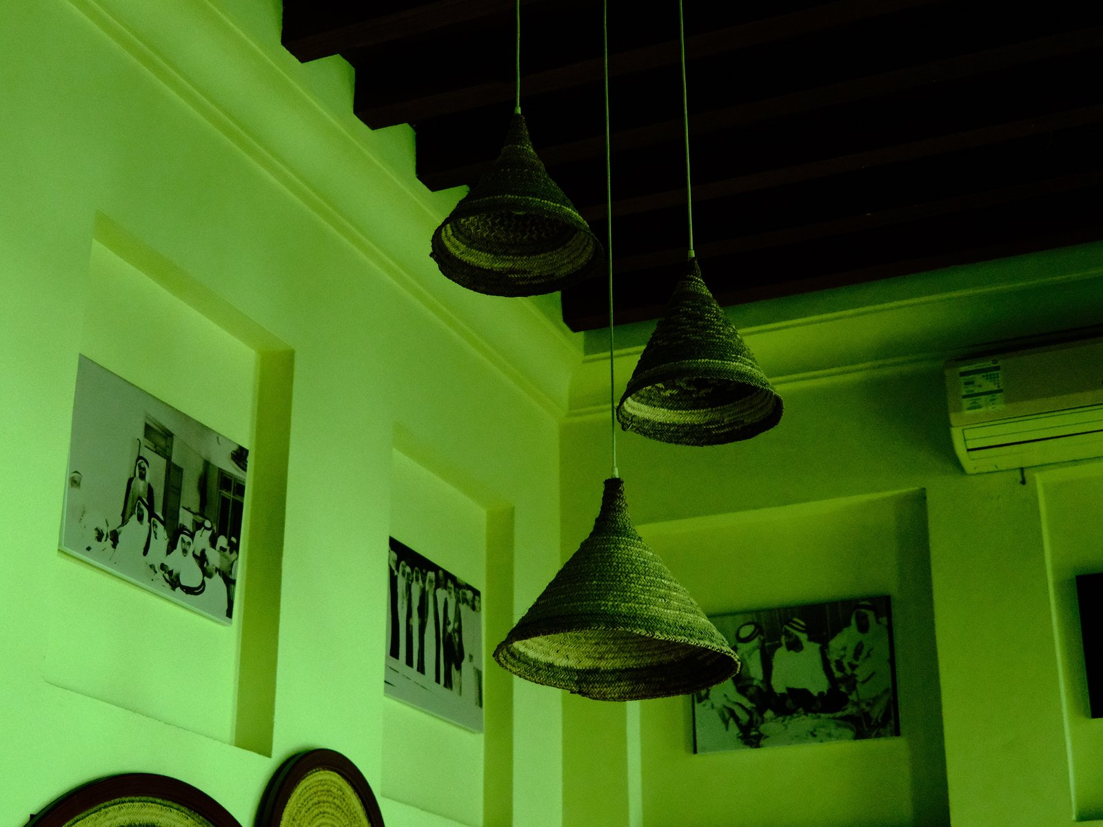 Three hanging light fixtures in a green-lit room with framed photographs on the walls.