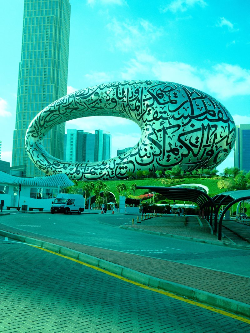 A large, modern sculpture with Arabic calligraphy in an urban setting, surrounded by buildings.