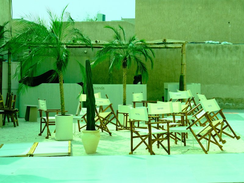 A rooftop scene with empty chairs, palm trees, and a light green hue.