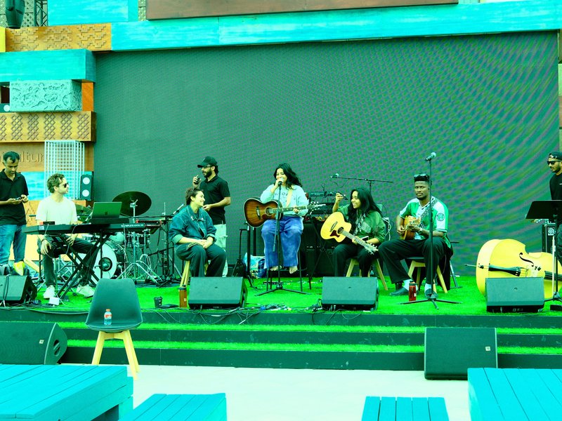 A group of musicians performing on stage with various instruments in a vibrant outdoor setting.