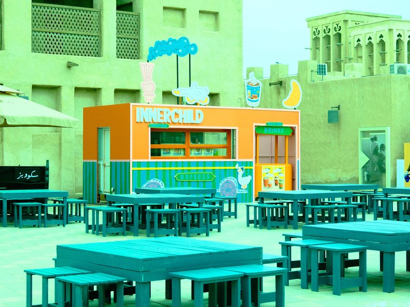 Colorful food stall in an outdoor setting with blue tables and a sandy backdrop.