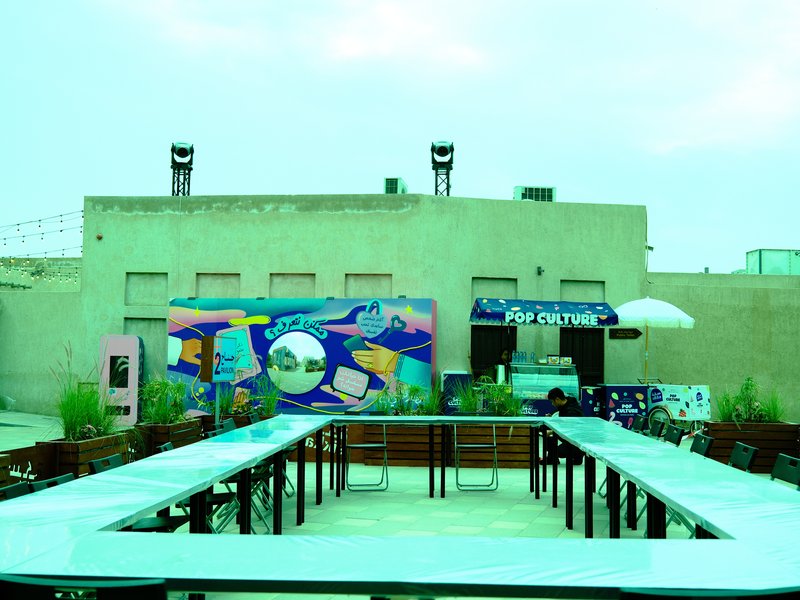 Outdoor venue with a mural, tables, and a stage under a cloudy sky.