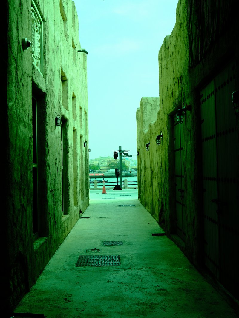 Narrow alleyway between textured walls leading to a distant view of a waterfront.