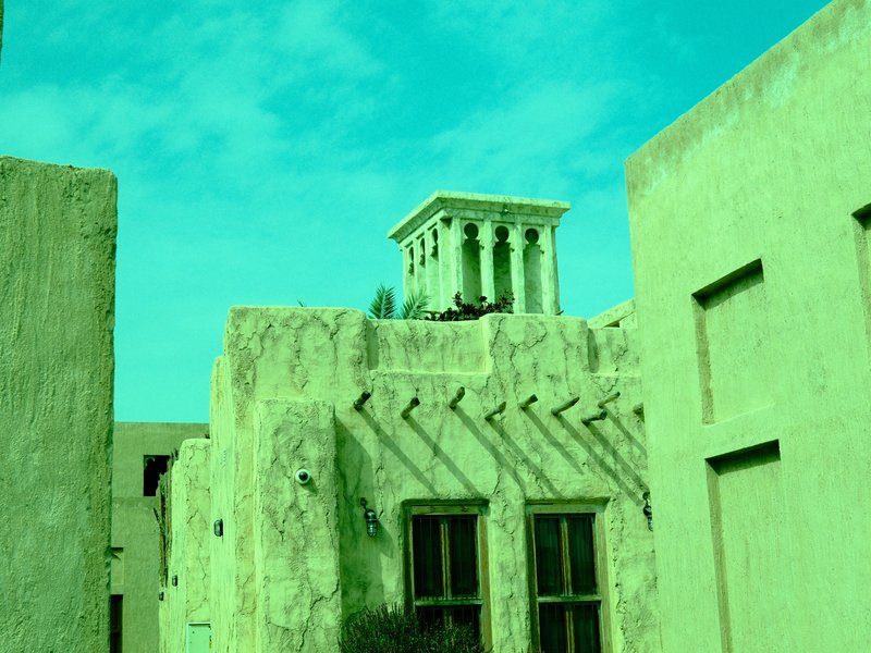 A unique architectural structure with a tower, surrounded by textured walls under a turquoise sky.