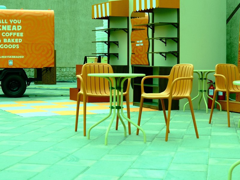Outdoor café scene with orange chairs and a green table, featuring a food truck in the background.