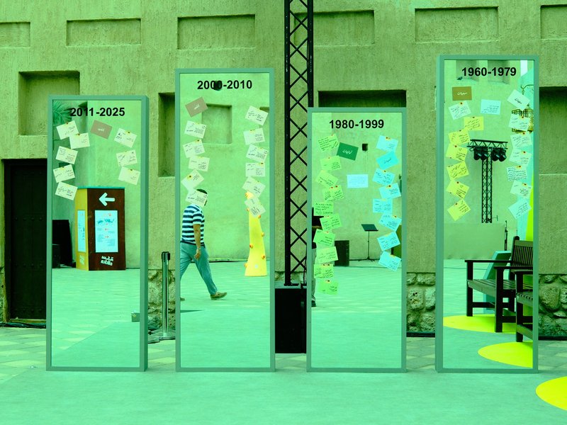 A series of four tall mirrors reflecting a person walking, with colorful notes attached to them.