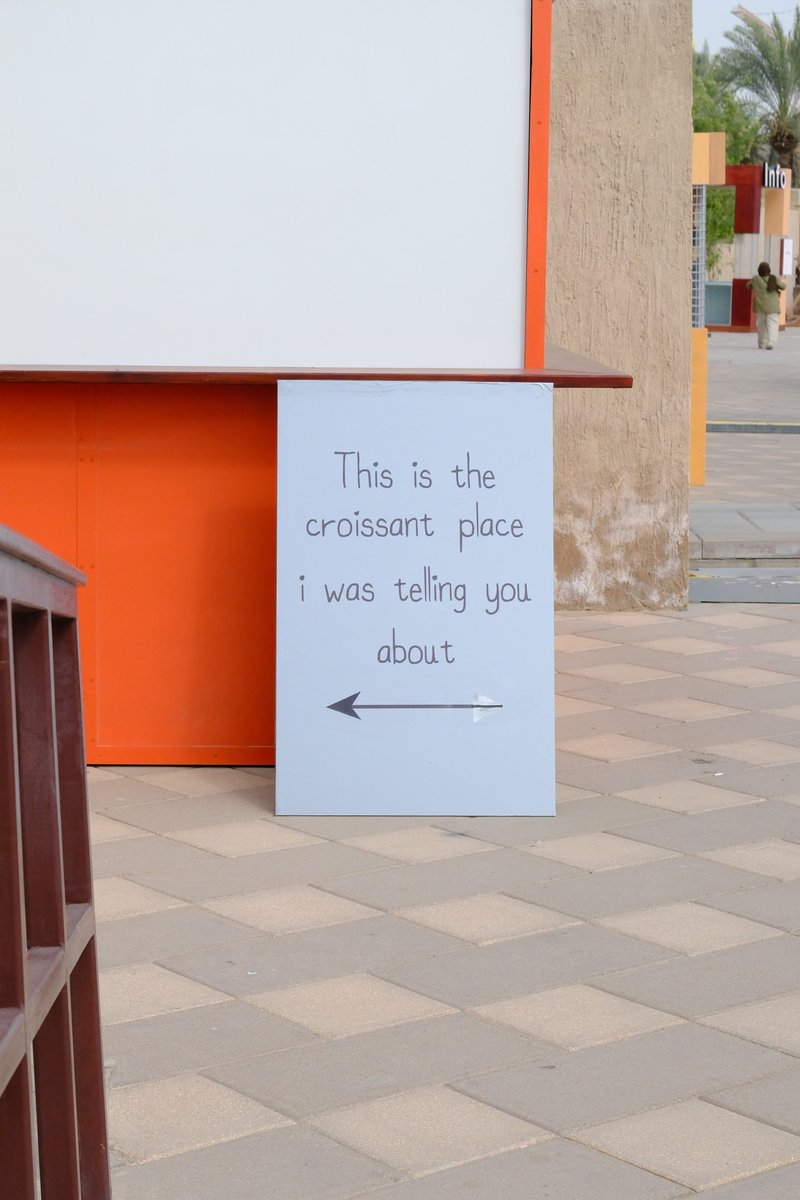 A sign pointing left, indicating a croissant place, set against a colorful urban backdrop.