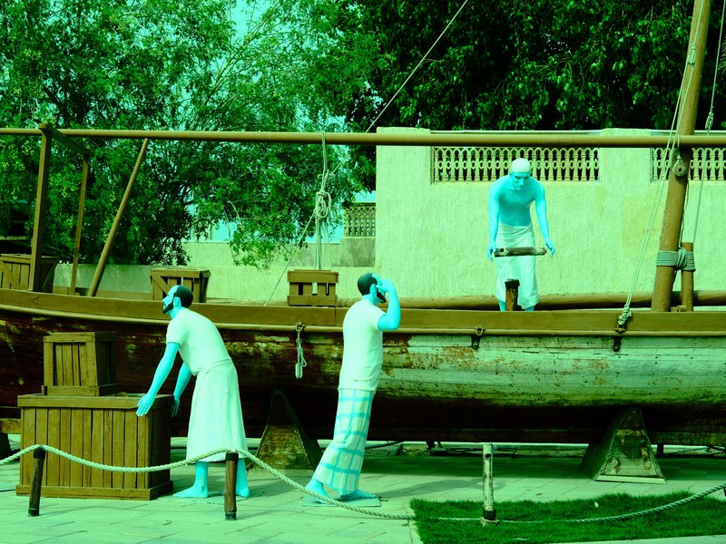 Three figures in blue attire interacting with a wooden boat in an outdoor setting.