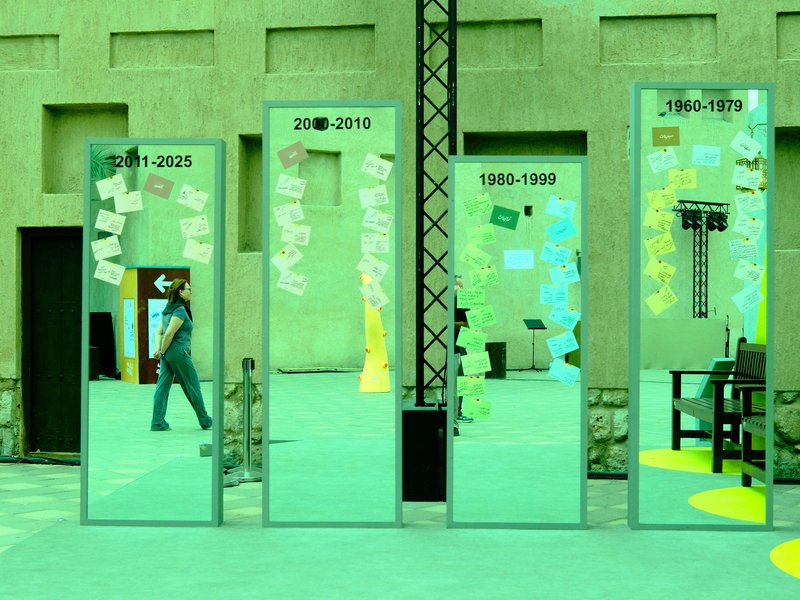 A series of mirrors reflecting a colorful installation with sticky notes and a chair in an urban setting.