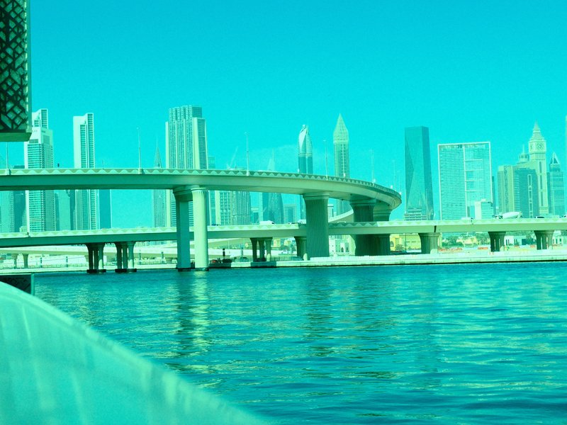 A view of a modern city skyline with a curved bridge over a shimmering body of water.