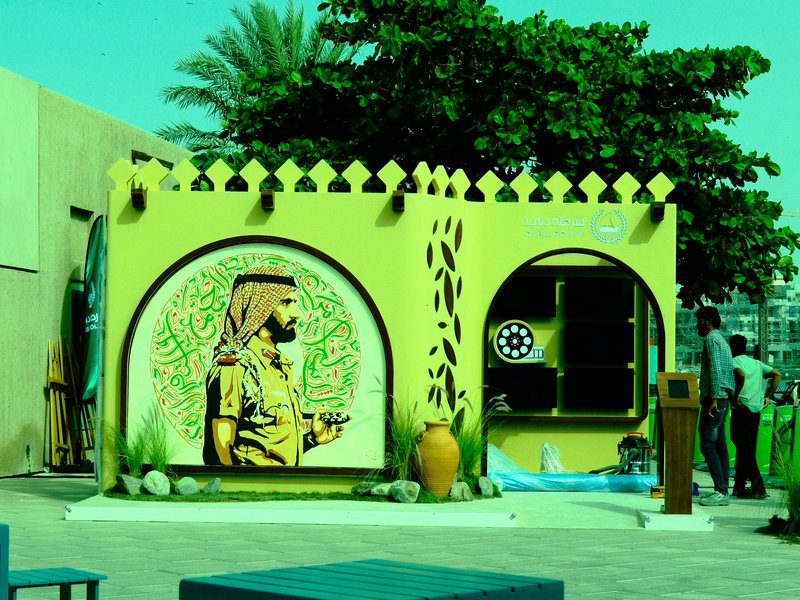 A vibrant mural of a man in traditional attire against a colorful wall with greenery and decorative elements.