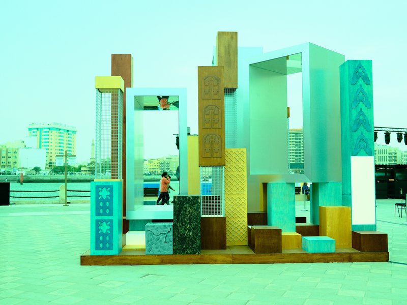 Colorful abstract sculpture in an urban waterfront setting with buildings in the background.
