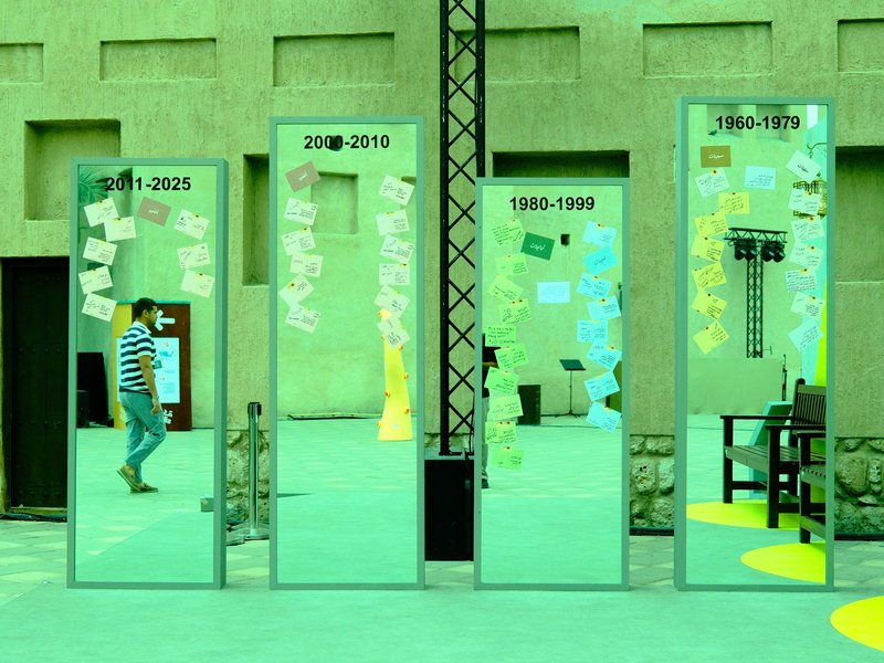 A man walking past four mirrored panels displaying different years and colorful notes in a green setting.