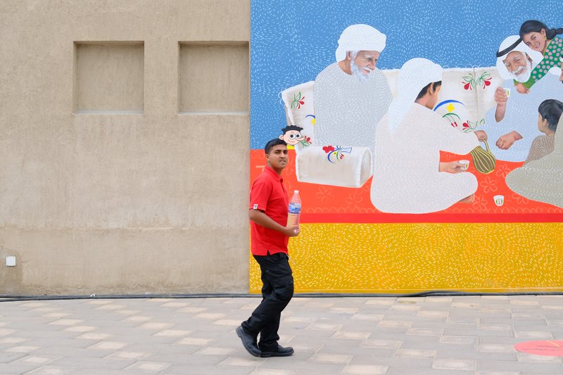A man in a red shirt walks past a colorful mural depicting people engaged in traditional activities.
