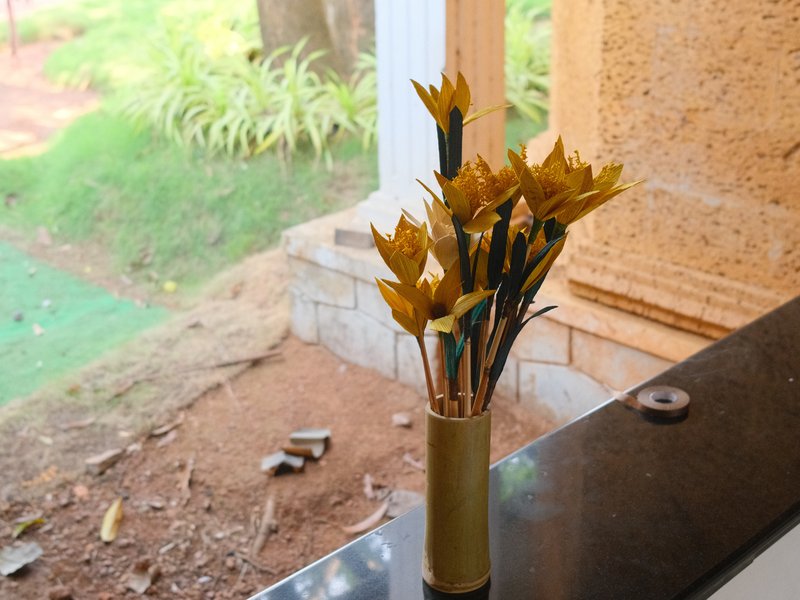 A vase with yellow flowers placed on a black surface near a window with natural light.