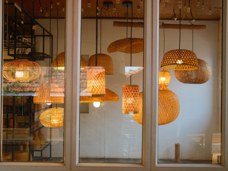 A collection of woven pendant lights hanging in a bright indoor space, viewed through a window.