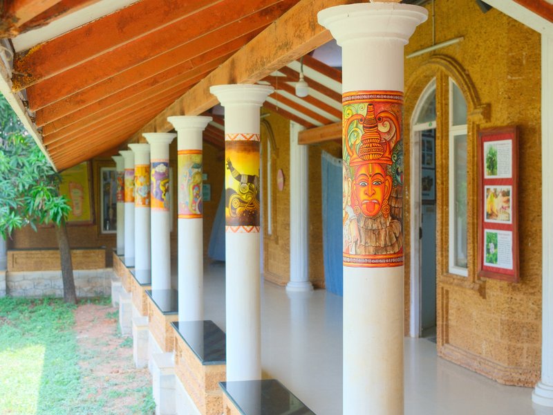 A corridor with decorative columns and artwork on the walls, surrounded by greenery.