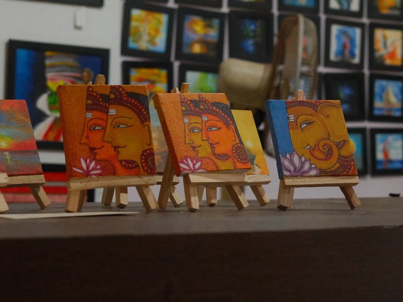 Colorful small paintings on easels in an art gallery, with more artwork in the background.