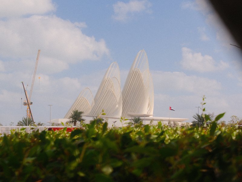 Three large, white architectural structures resembling petals against a blue sky with clouds.