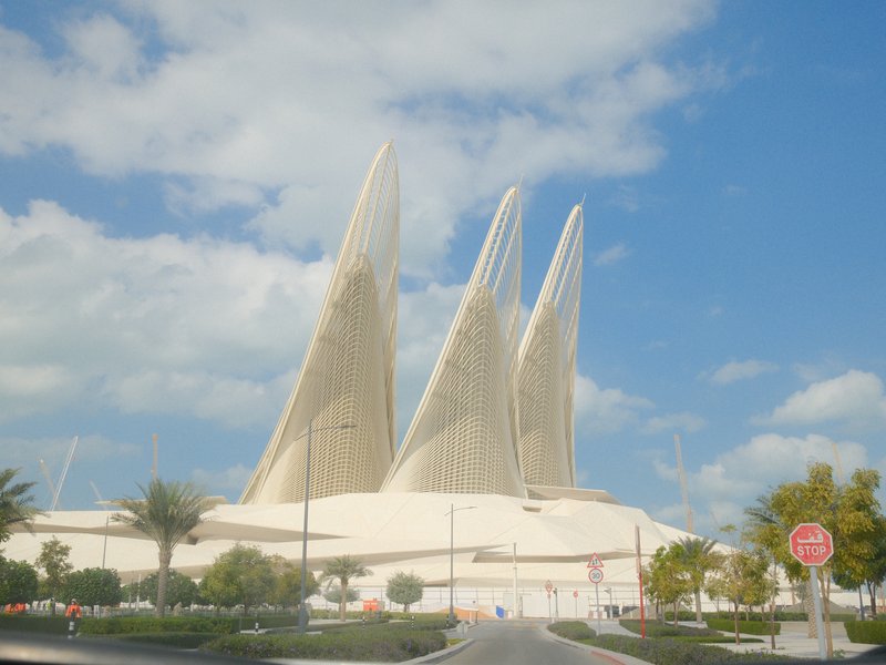 Three large, sail-like architectural structures against a blue sky with scattered clouds.