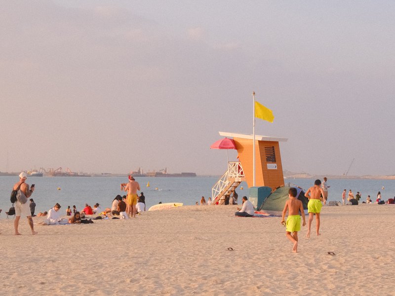 Beach scene with lifeguard tower, people relaxing on sand, and children playing near the water.