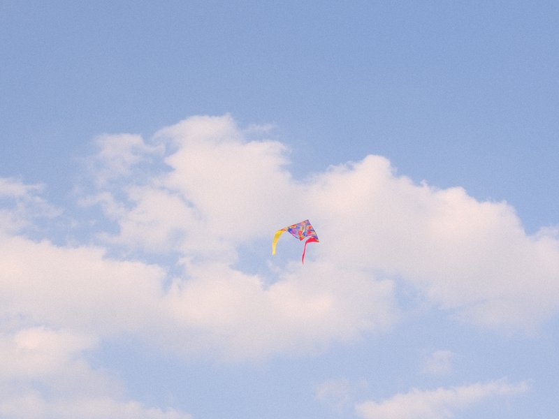 A colorful kite soaring in a blue sky with fluffy white clouds.