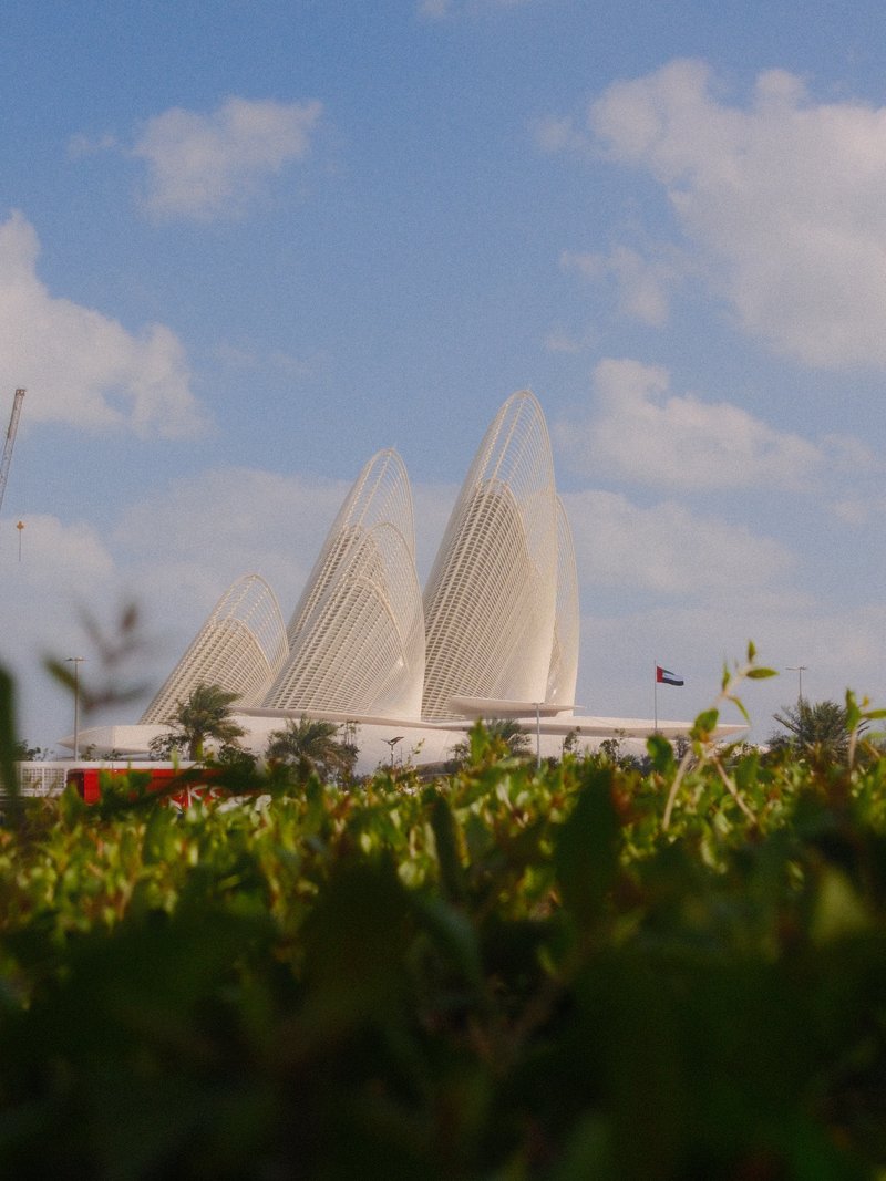 Three distinctive white architectural structures rise above green foliage under a blue sky with clouds.