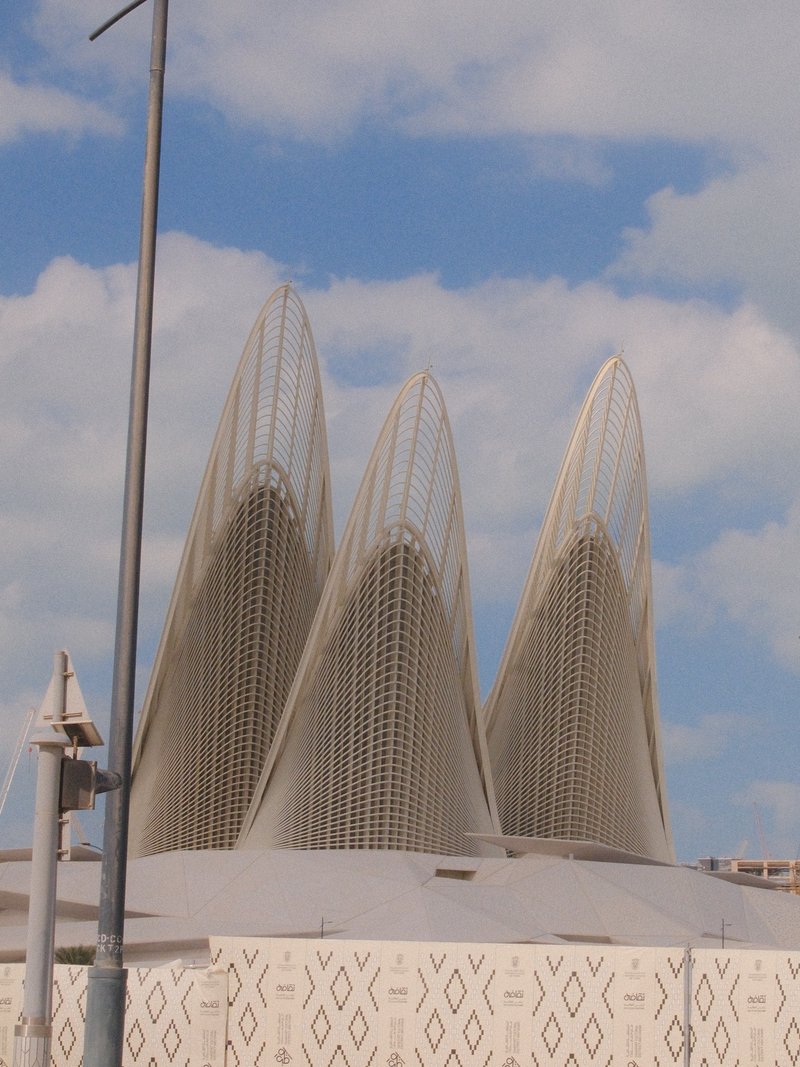 Three distinctive architectural structures with pointed tops against a cloudy sky.