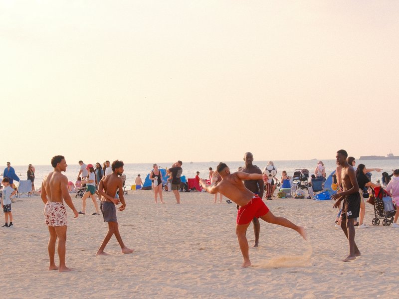 Group of young men playing beach volleyball on a sandy beach during sunset.