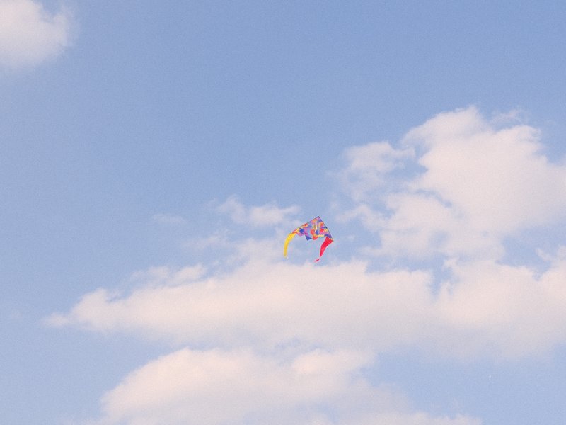 A colorful kite flying high in a blue sky with fluffy white clouds.