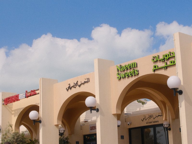 Architectural view of a shopping plaza with arched entrances and decorative signage under a blue sky.