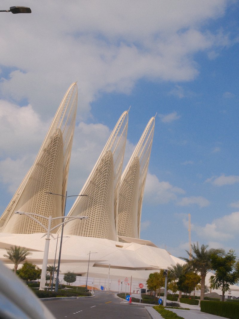 Architectural structure with three tall, pointed elements against a blue sky with clouds.