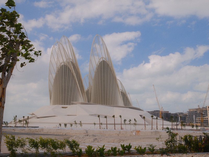 A modern architectural structure resembling two large petals against a blue sky with scattered clouds.