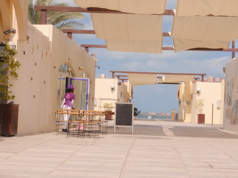 A quiet outdoor cafe scene with tables and chairs under fabric awnings, leading to a coastal view.