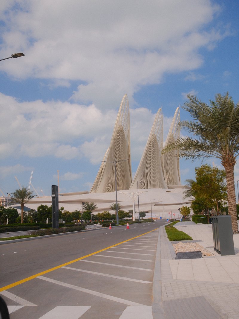 Modern architectural structure with large, sail-like features against a blue sky and palm trees.