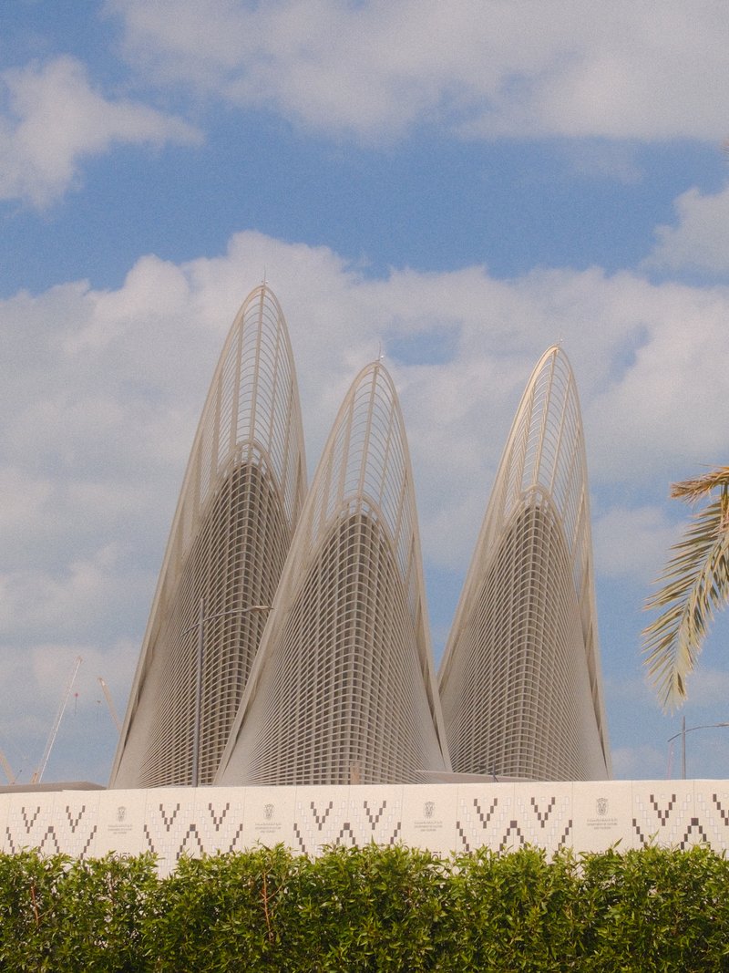 Three architectural structures with a mesh design against a blue sky with clouds.