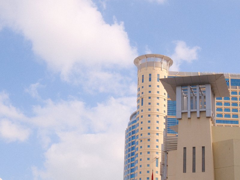 A modern building with a cylindrical tower against a blue sky with fluffy clouds.