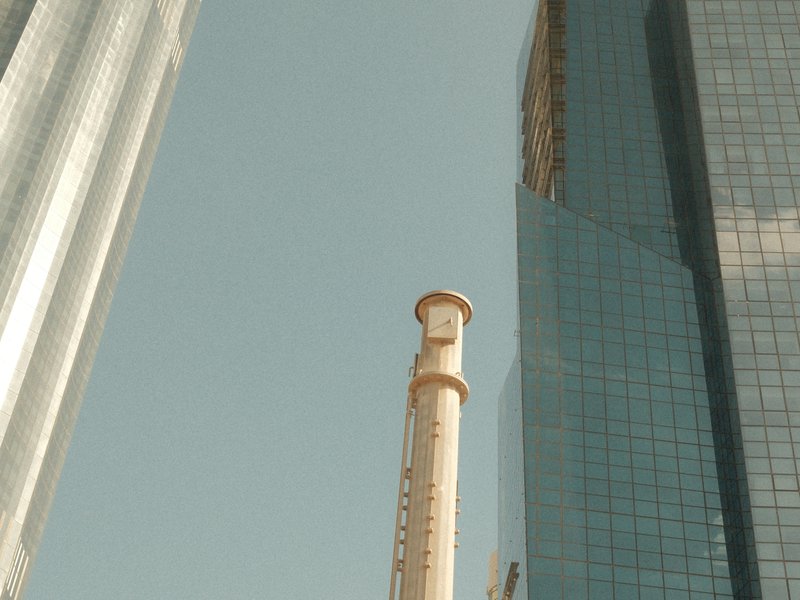 Tall buildings with a smokestack in between, under a clear blue sky.