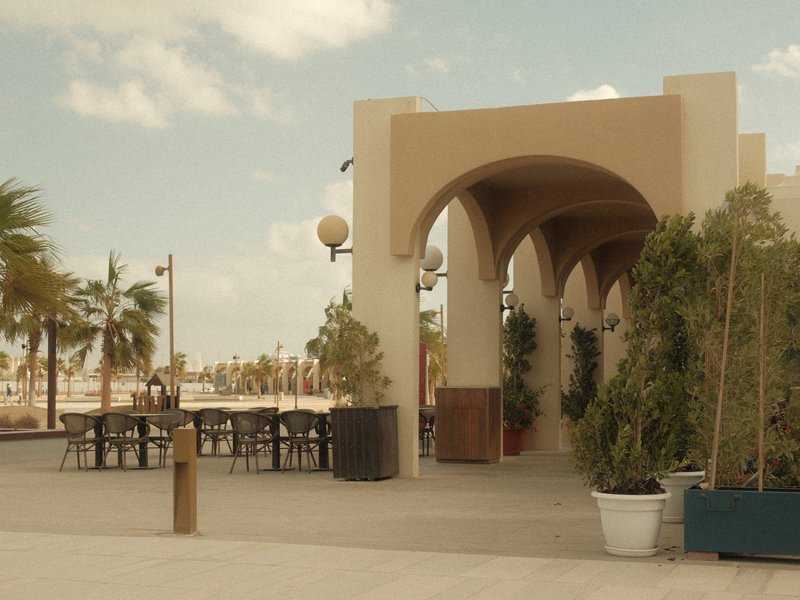 A coastal promenade with arches, palm trees, and outdoor seating under a clear sky.
