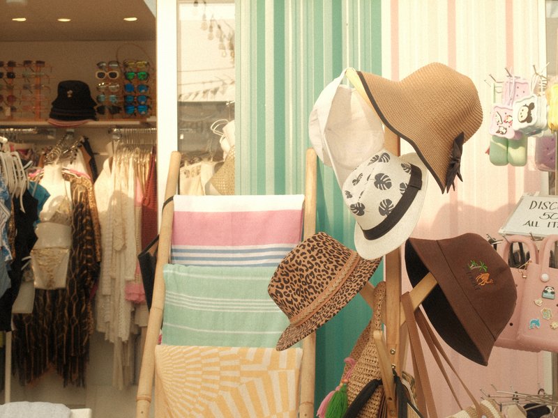 A display of various hats in a boutique with colorful striped walls and clothing in the background.
