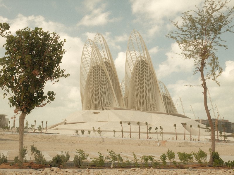 A modern architectural structure resembling petals, surrounded by sparse greenery and a cloudy sky.