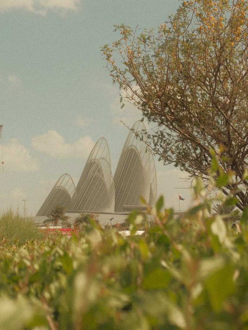 Three distinctive architectural structures rise above greenery under a blue sky with scattered clouds.