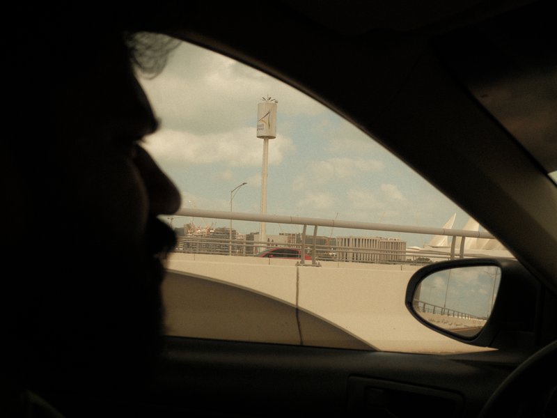 Silhouette of a person in a car with a cityscape visible through the window.