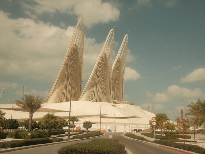 A modern architectural structure with three sail-like features against a blue sky with clouds.