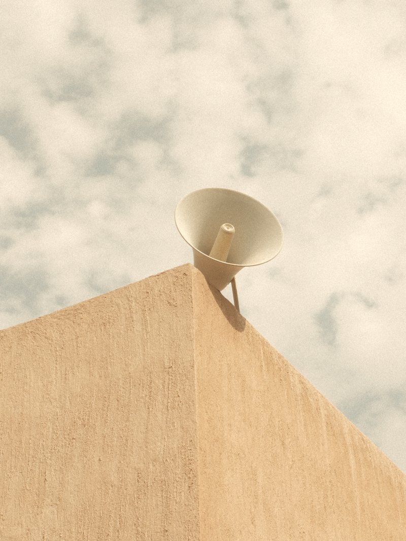 A megaphone mounted on a beige wall under a cloudy sky.